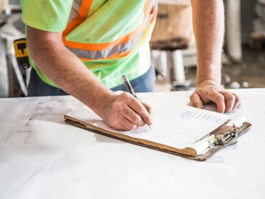 Consultant in a safety vest writing notes on a clipboard