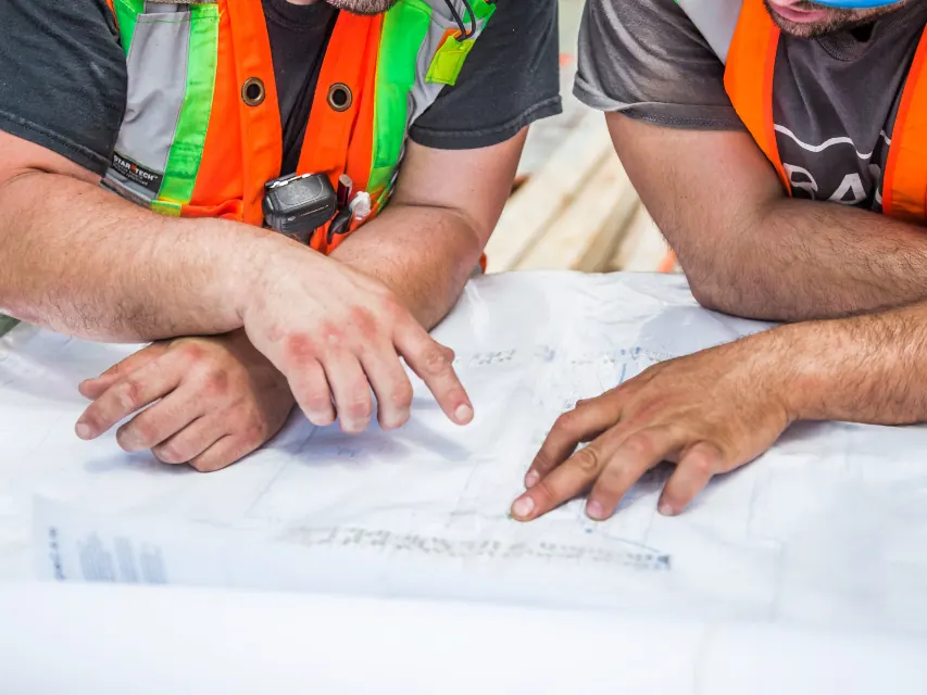 Two installers in safety vests reviewing solar plans on a table