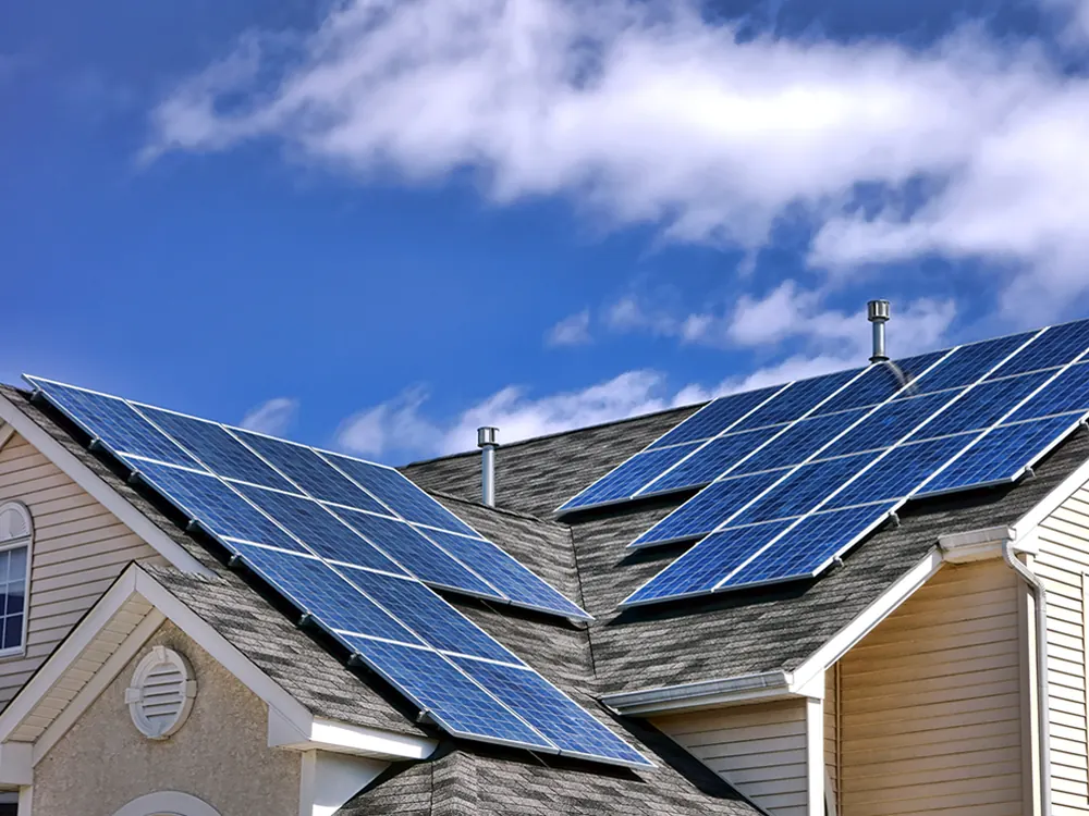 Two-story home with dark solar panels on the roof under a bright blue sky