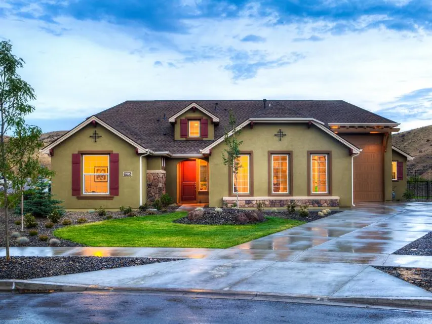 Single-story home with lit windows and a wet driveway after rain