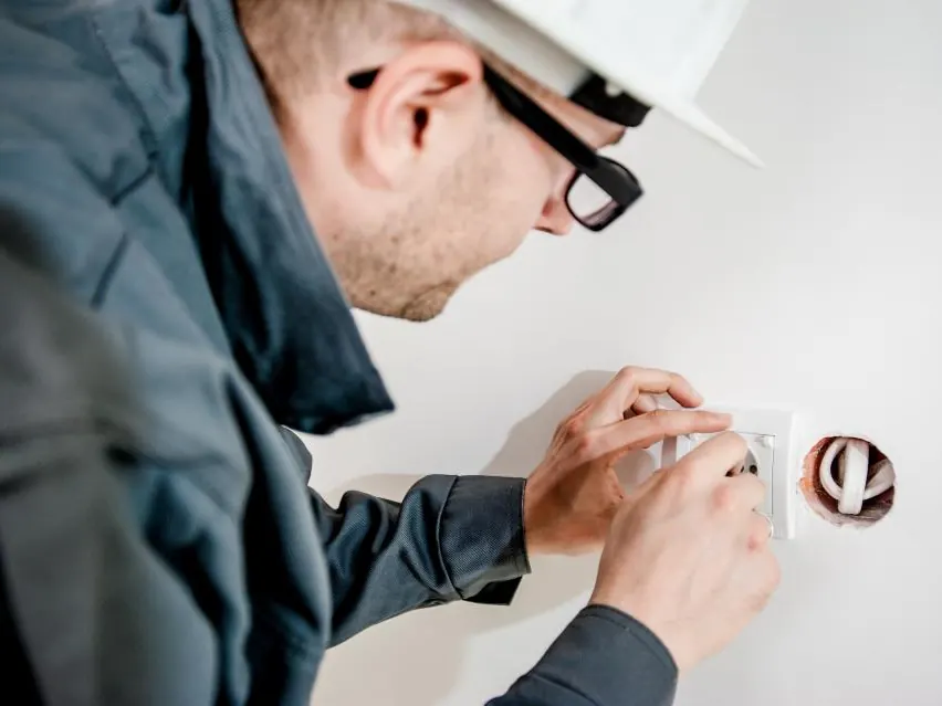 Technician in a hard hat and safety glasses checking a wall fitting